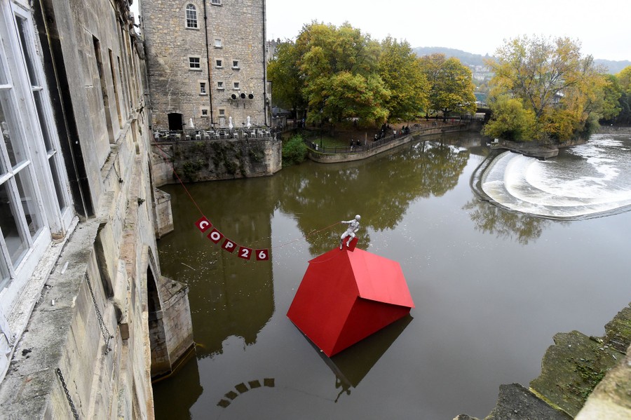 A model of a small red house appears to be sinking in a river.