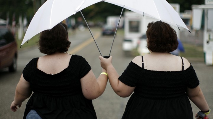 Two women dressed in black dresses holding white umbrellas