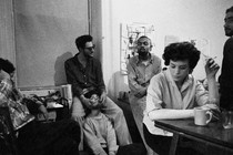 A black and white photo of writers sitting around at a party smoking and drinking