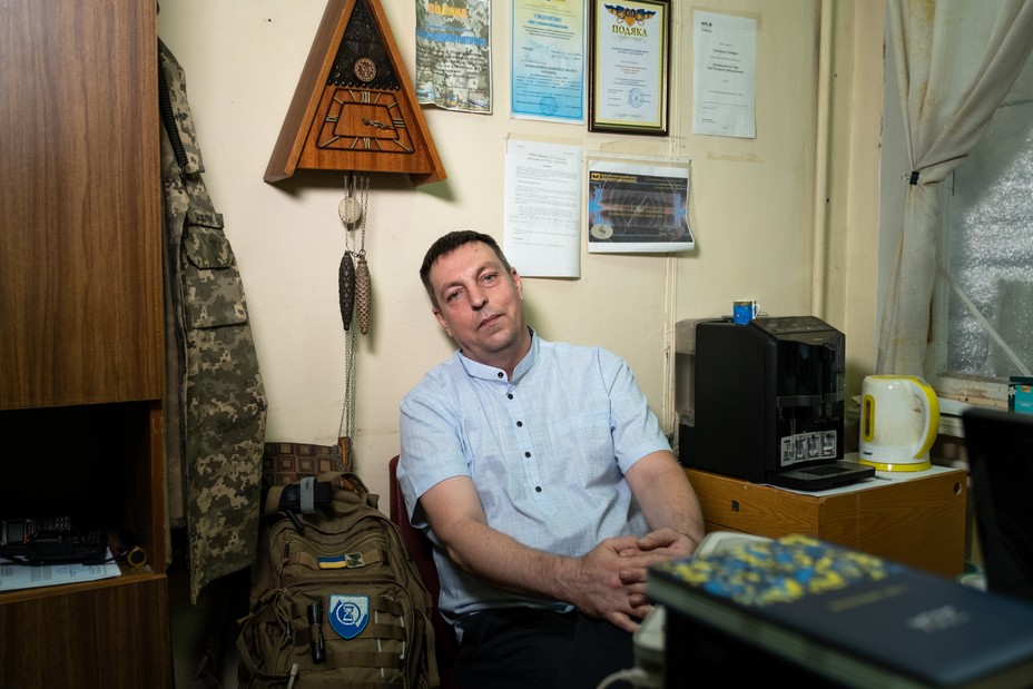 A man wearing a light blue shirt sits in a chair against the wall in an office.