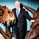 Newt Gingrich stands, grinning, between exhibits of dinosaur skeletons.