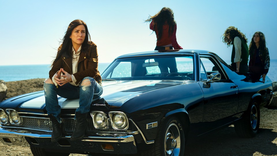 Pamela Adlon, as Sam, sits on the hood of a car with her three kids playing behind her