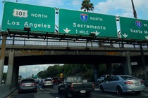 Morning traffic makes its way along a freeway interchange in Los Angeles. The traffic signs read Los Angeles, Sacramento, and Santa Monica.