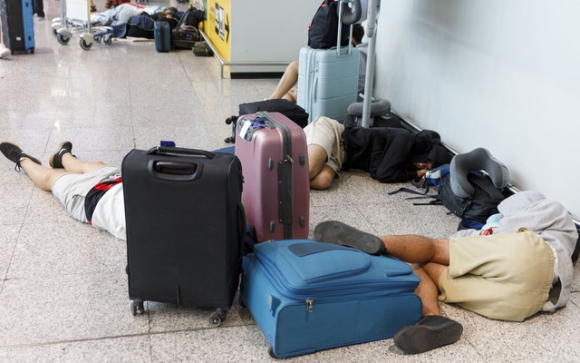 people sprawled out on an airport floor, along with carry-on suitcases