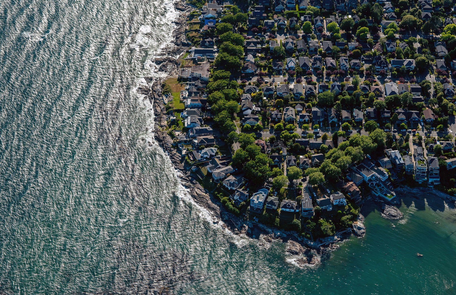 An aerial view of homes built along a rocky coastline in a dense neighborhood