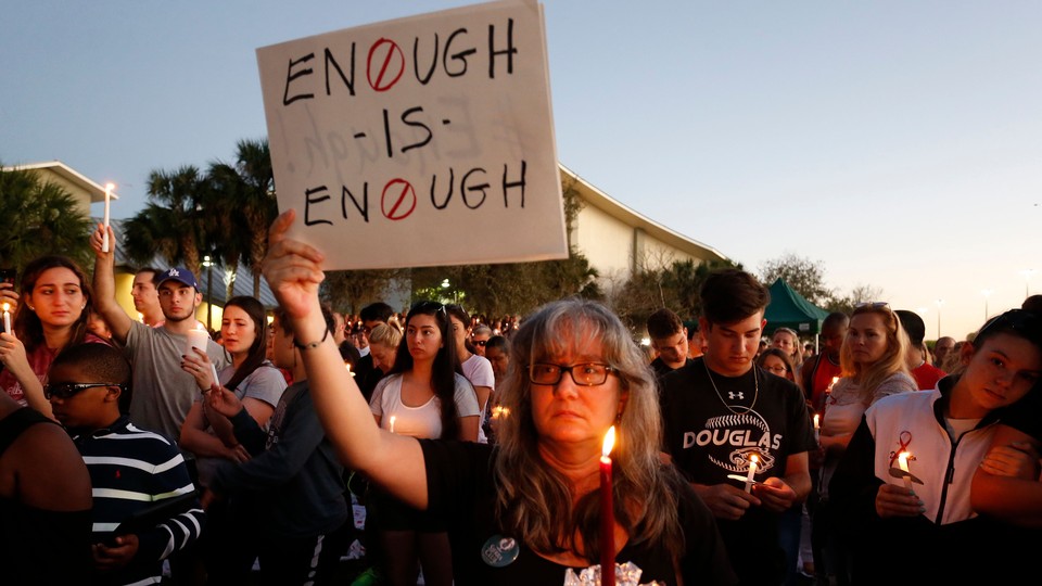 People hold candles at a rally and a woman holds a sign that reads "Enough is enough."