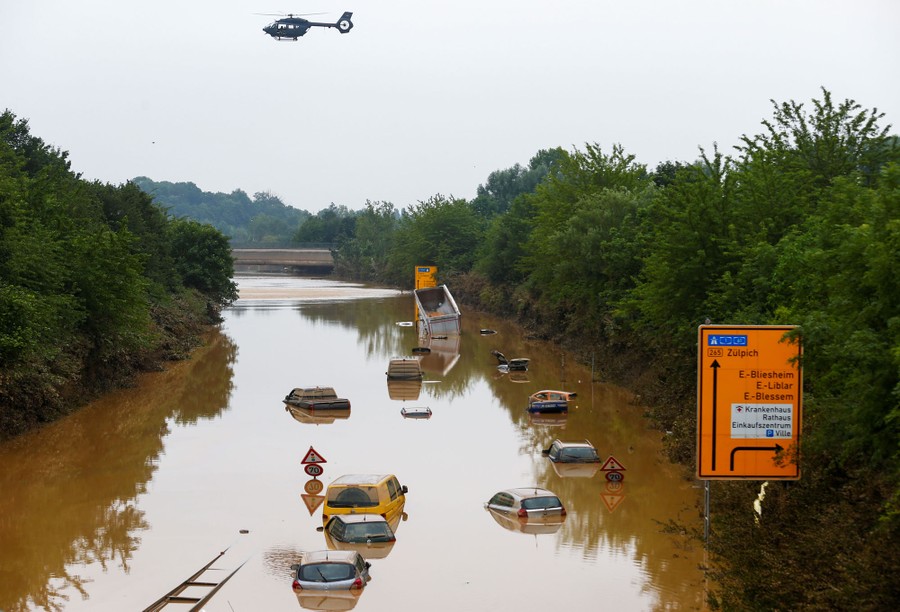 A helicopter flies above cars partially submerged in floodwater.