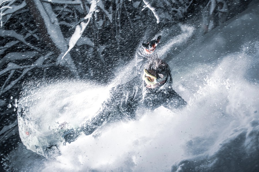 An athlete plows through snow, sending it flying around him.