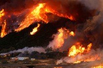 Flames whipped by strong winds burn though a hillside before destroying camper vans during the Blue Cut fire.