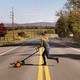 photo of woman with long hair pushing hand mower across rural two-lane road with mountains in background