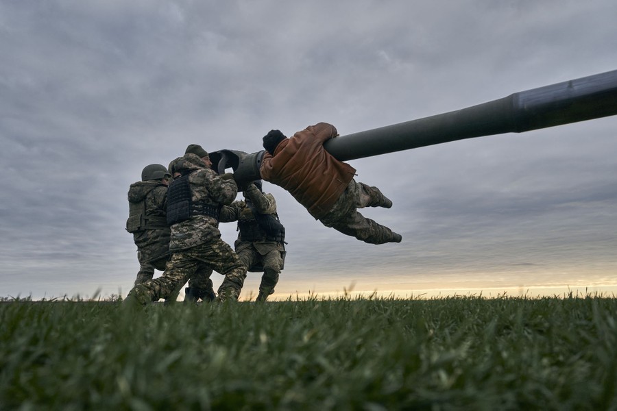 Several soldiers struggle with the barrel of a large piece of artillery.