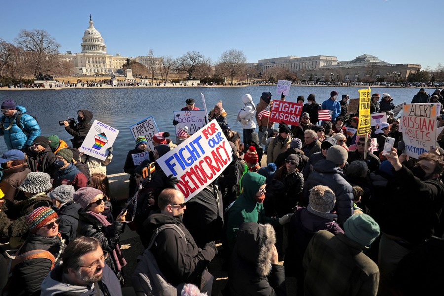 A group of demonstrators gather by a reflecting pool near the U.S. Capitol Building.