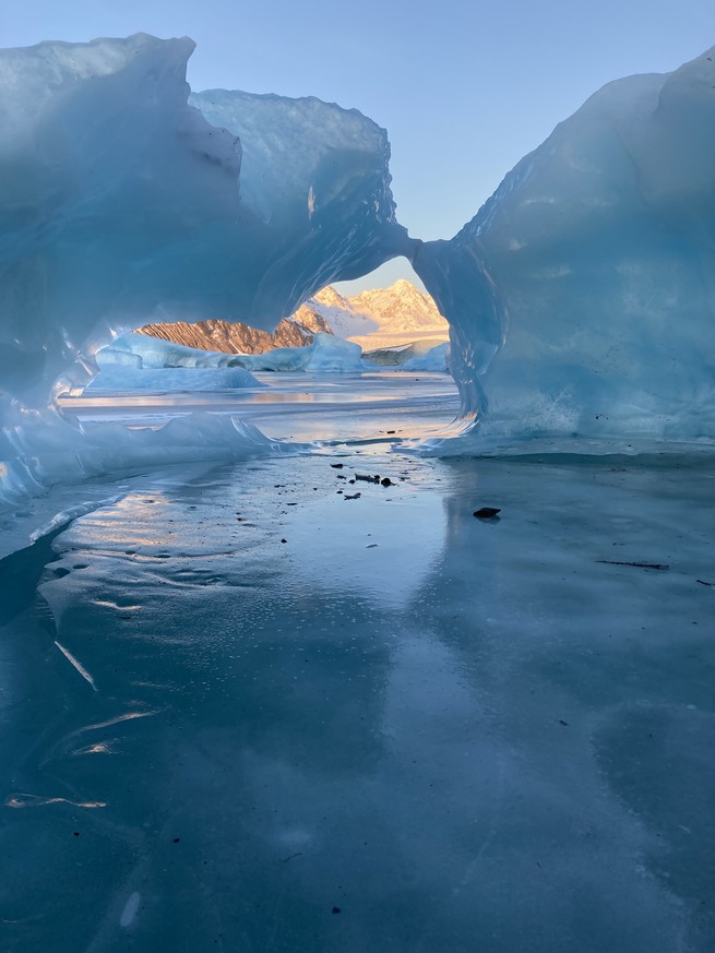 A view of a distant purple mountain through an arch of glacial blue ice