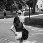 A black-and-white photo of a young woman, seen from behind, wearing a backpack and walking on a campus