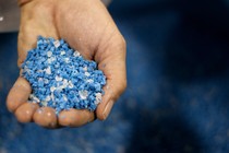 A hand holding a scoop of irregular blue plastic pellets, called nurdles