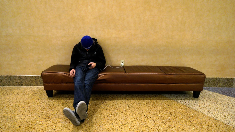 A man sleeps on a couch with his cell phone plugged into a nearby outlet
