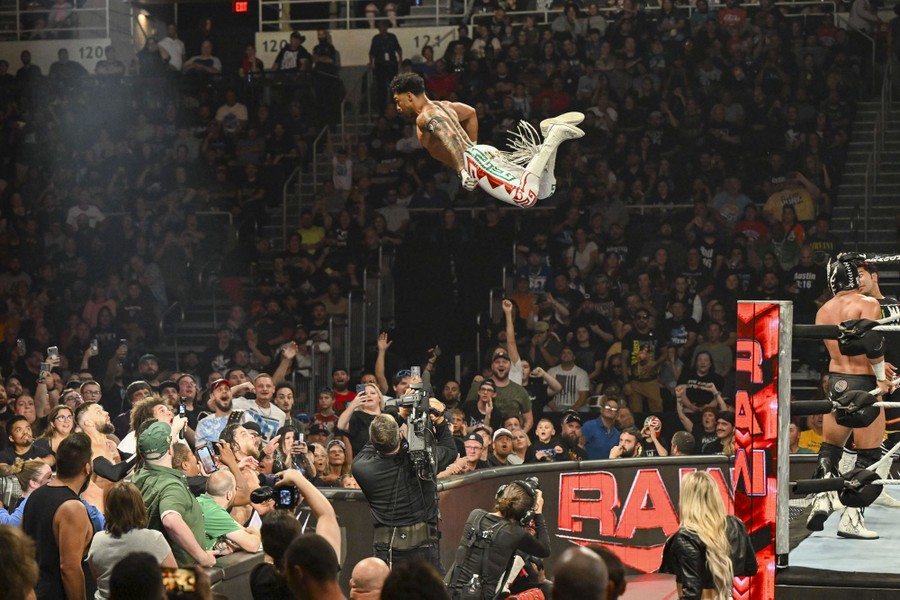 A wrestler makes a high jump from the top of the ropes toward a crowd.