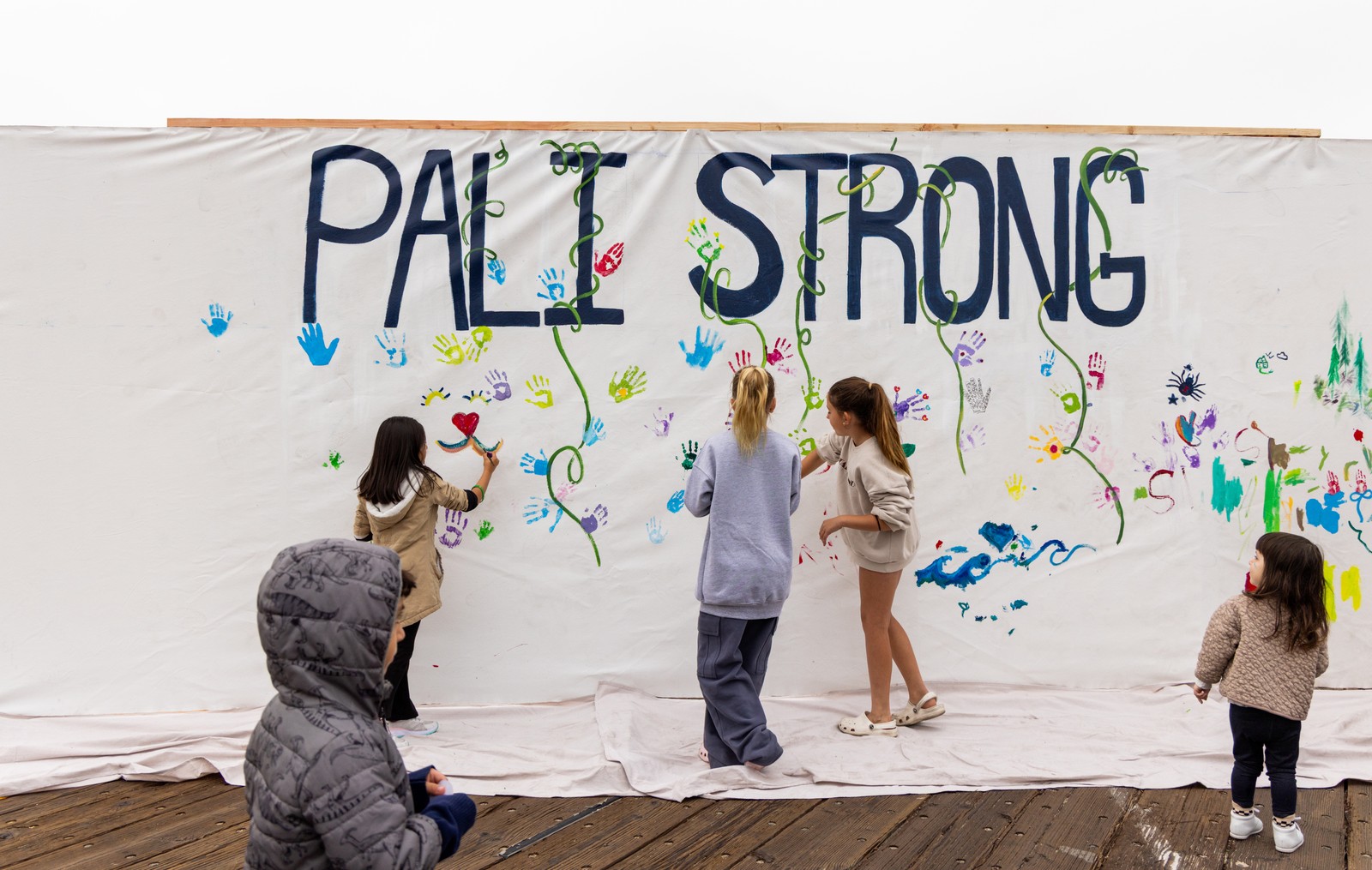 Several children paint on a large canvas that reads