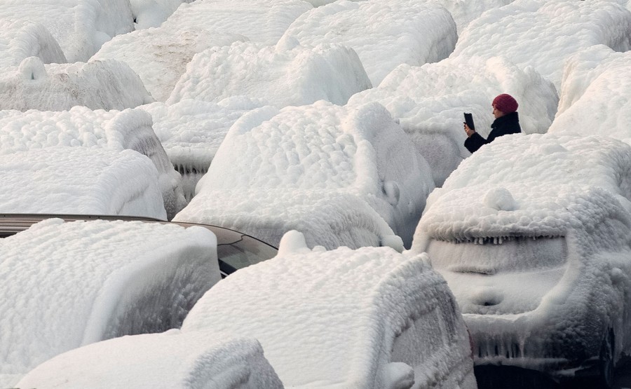 A woman takes a picture of several completely ice-covered vehicles.