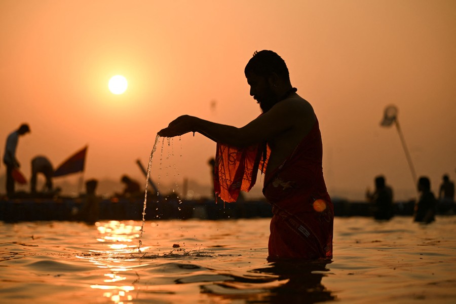 A worshipper stands knee-deep in a river, dripping water from their outstretched hands.