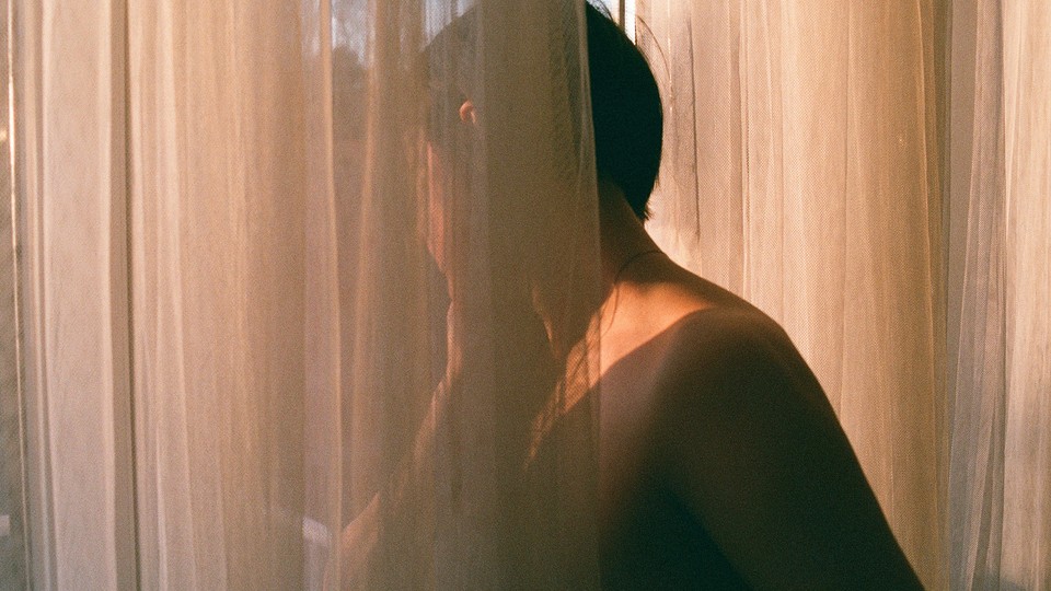 A person looking out a window behind a gauzy curtain