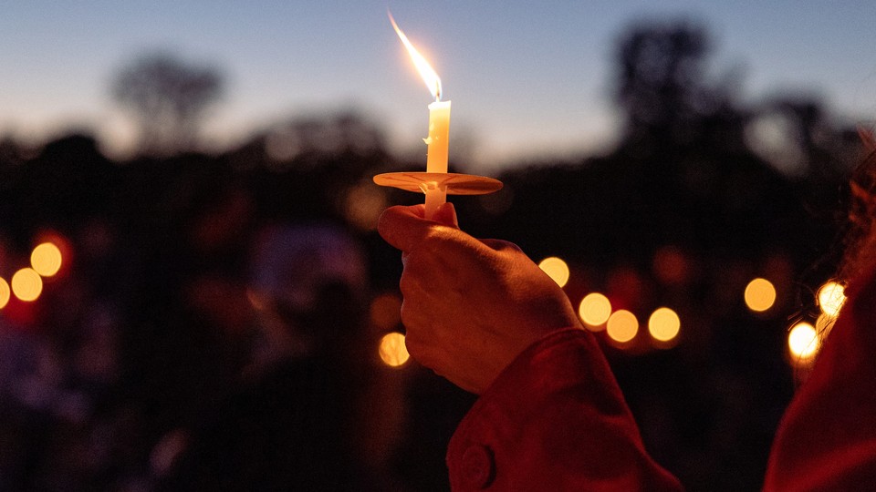 Color photograph of a single candle being held aloft at a vigil.