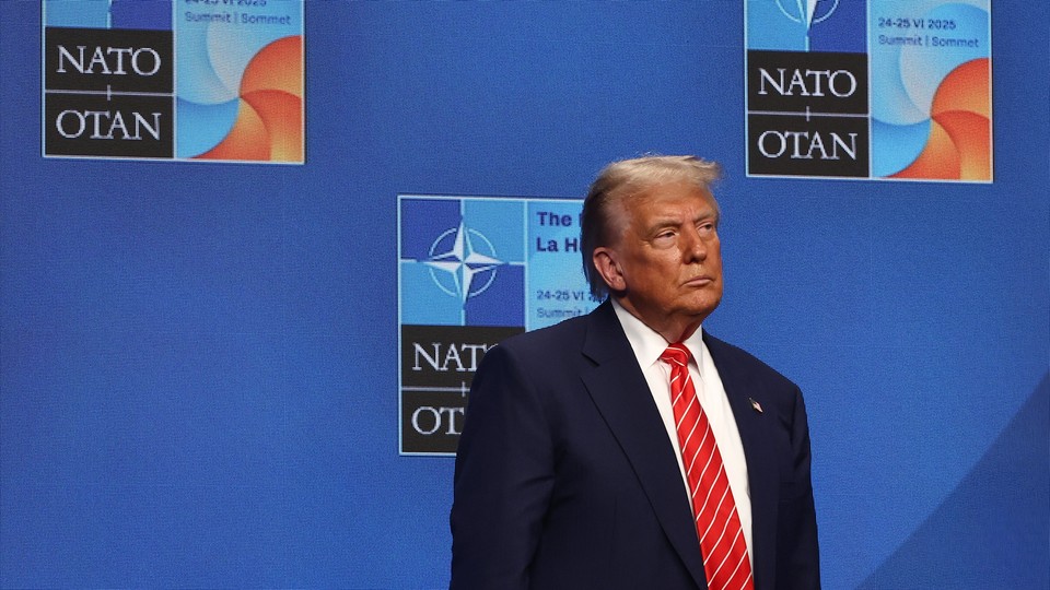 Trump stands alone at a NATO summit in front of a blue background