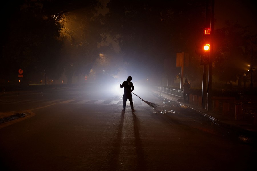 A man sweeps a road on a dark and smoggy night.