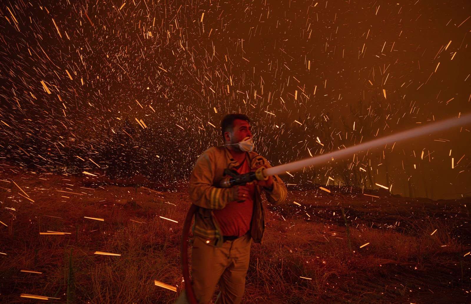 Flying embers fill the air, swirling around a firefighter spraying water from a hose.