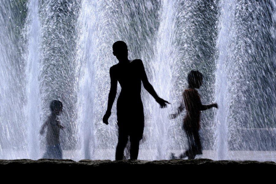 The silhouettes of three children playing in a fountain