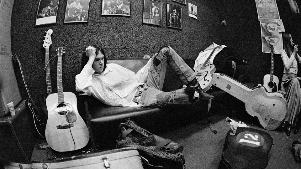 A young Neil Young lying sideways on a couch surrounded by guitars