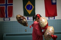 A student carrying balloons walks past the flags of Norway, Brazil, and Taiwan. 