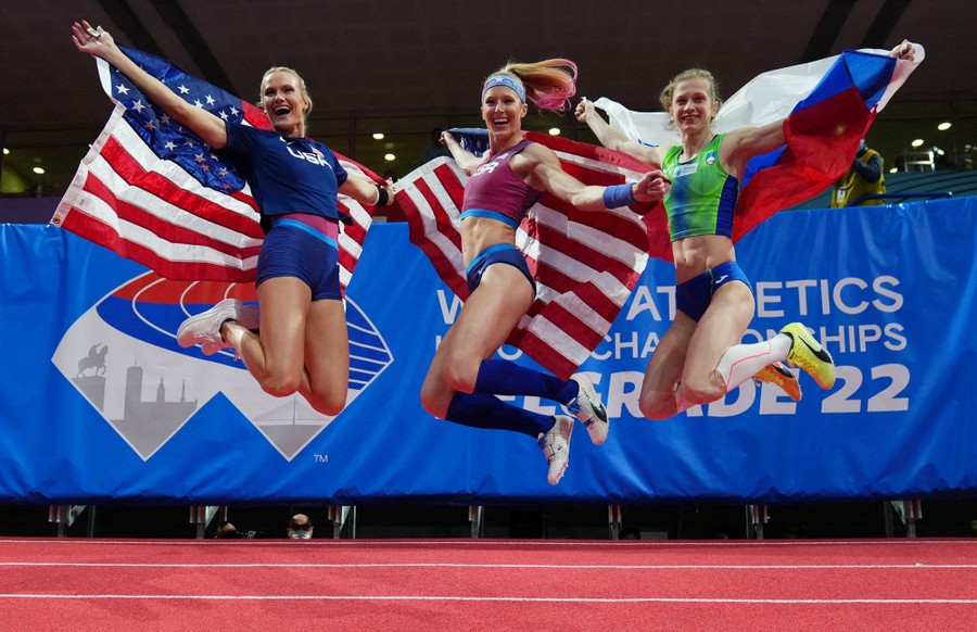 Three athletes jump in celebration on a track.