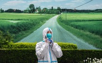 Photo of a Chinese health worker in a protective suit, against a backdrop picture of a country road