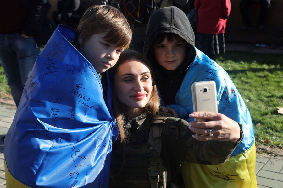 A woman and two boys wrapped in Ukrainian flags pose for a selfie.