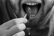 A close-up of a man putting a cooked cicada into his mouth