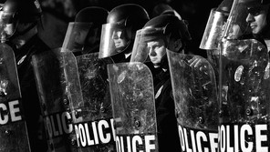 A black-and-white photo of a line of police officers with shields.