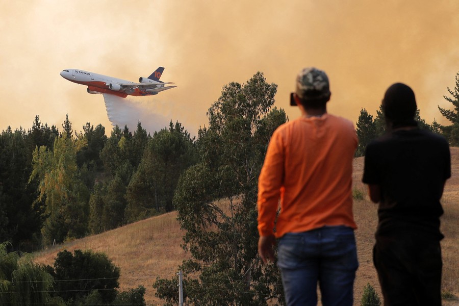 People watch as a plane drops water on a forest fire.
