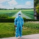A security guard wearing a Hazmat suit stands in front of a patch of green and a large photo of rolling fields in Beijing