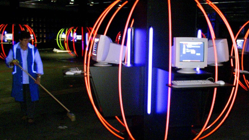 A person cleans up in a room full of computers and neon lights.