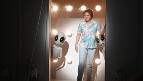 Kate McKinnon standing in the doorway of a spaceship with two gray aliens