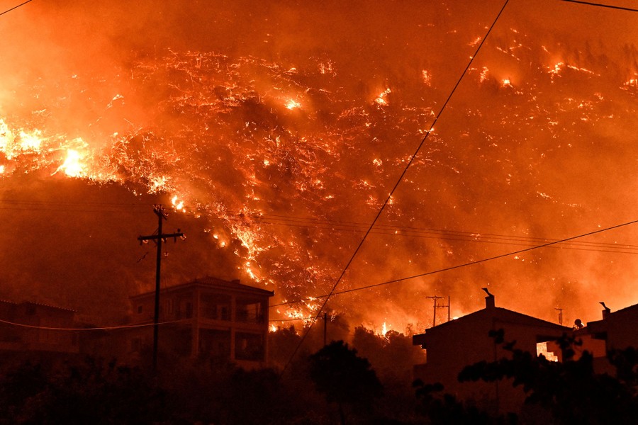 Houses on a hillside in silhouette, with a raging wildfire burning on the hill behind them