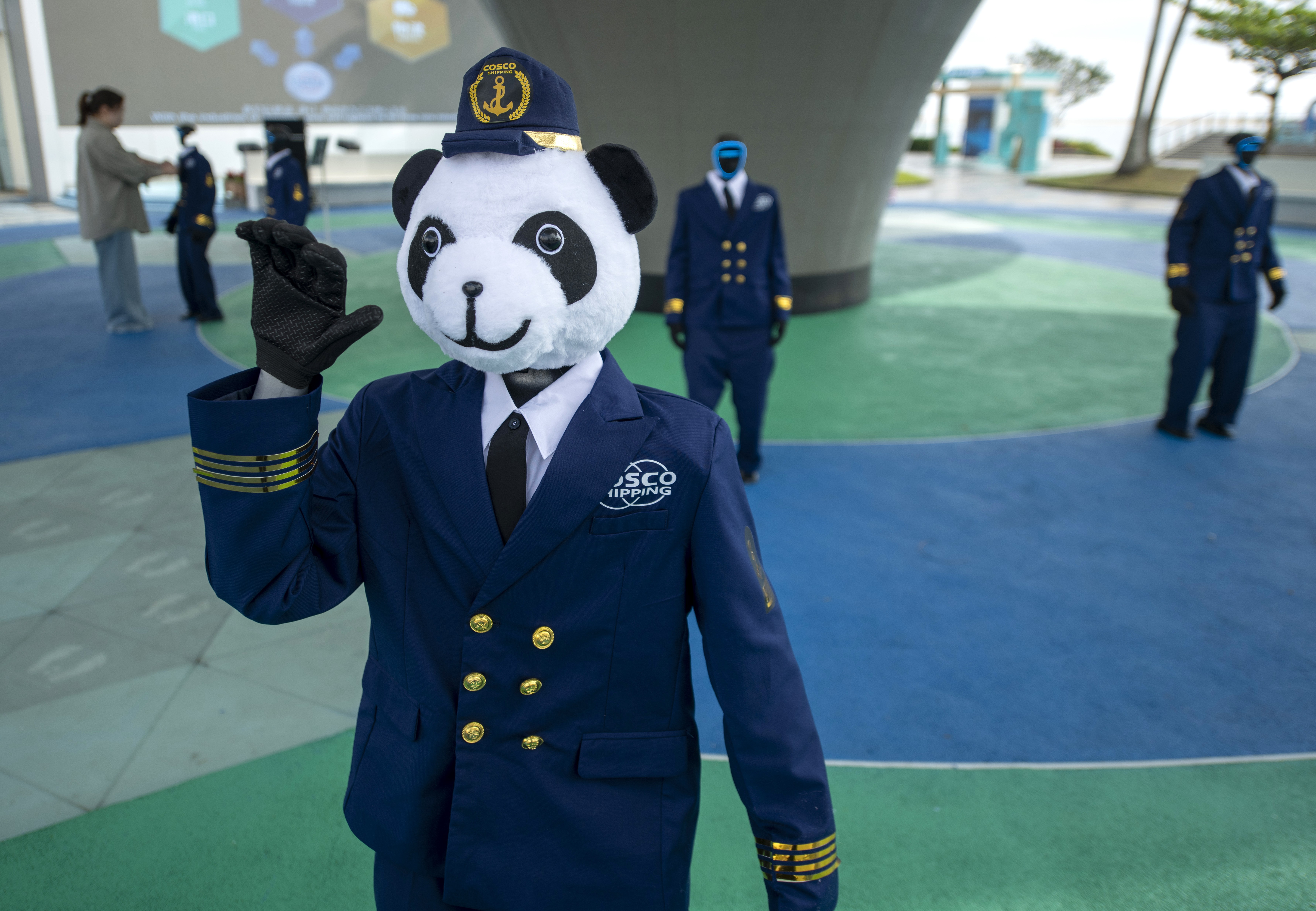 A humanoid robot wearing a uniform and a panda mascot head dances alongside several other uniformed robots.