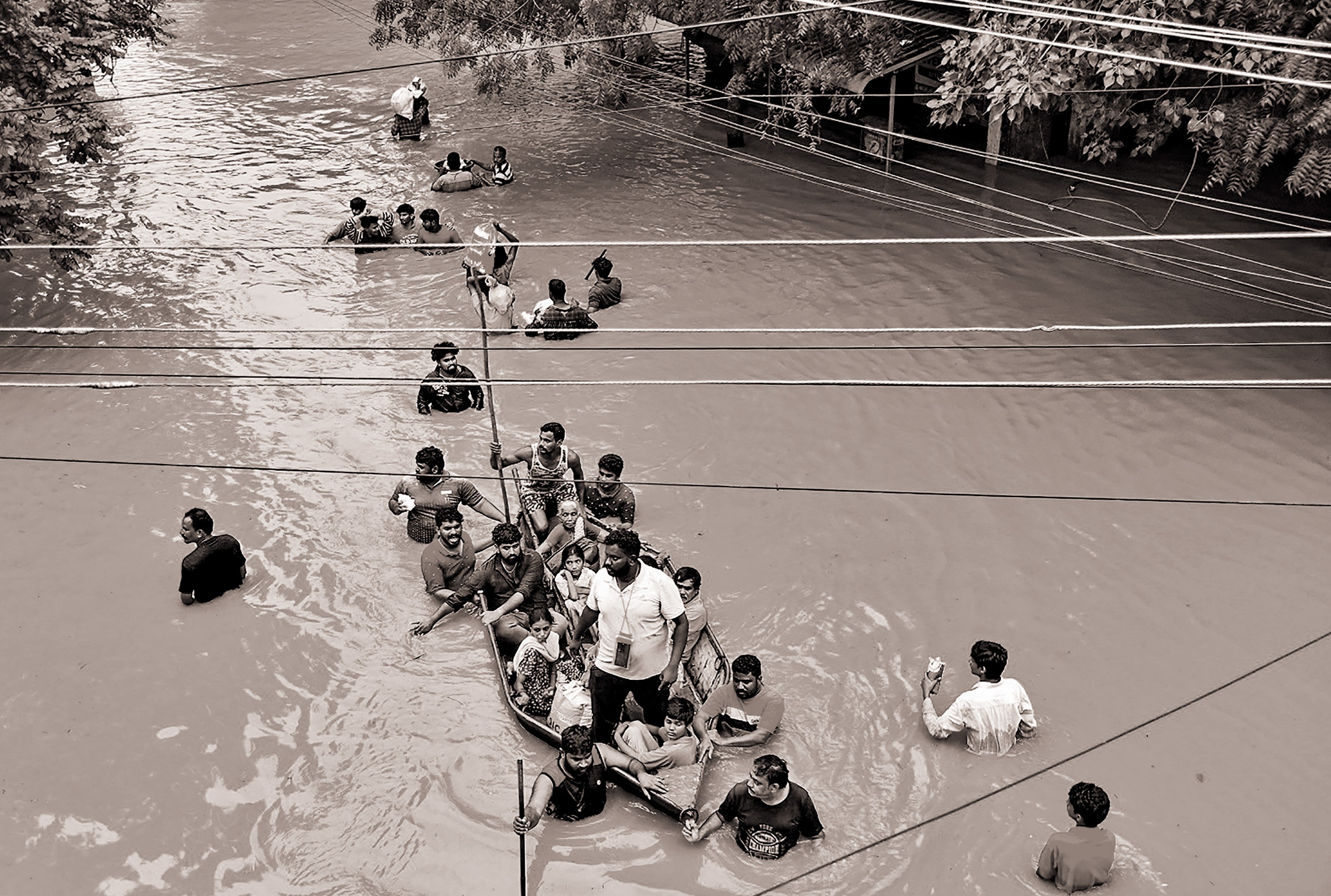 black-and-white photo of flooded road with people wading chest-deep, some pushing a boat full of people