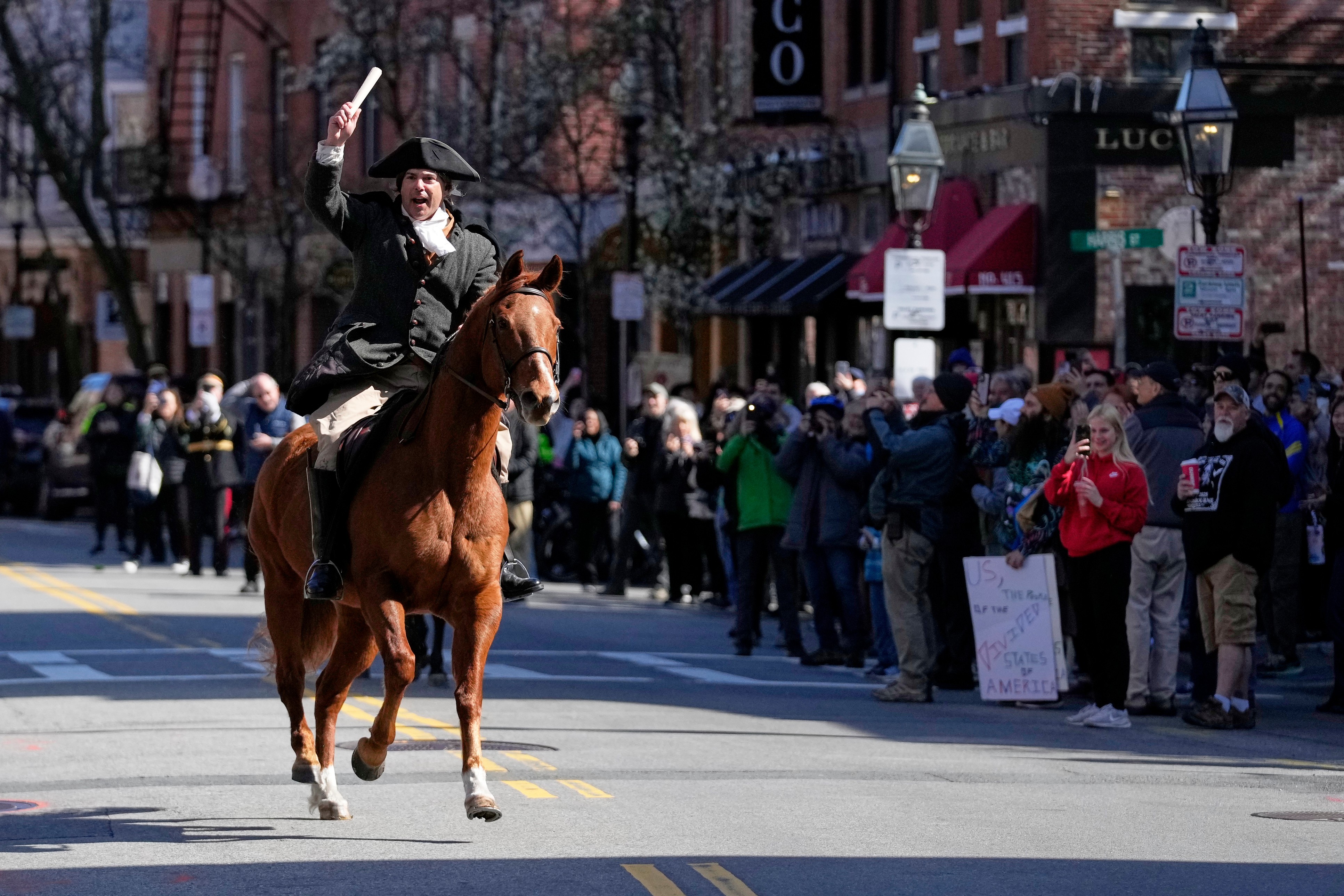 A person dressed as Paul Revere rides a horse past a crowd in Boston.