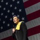 Elon Musk stands in front of a giant American flag