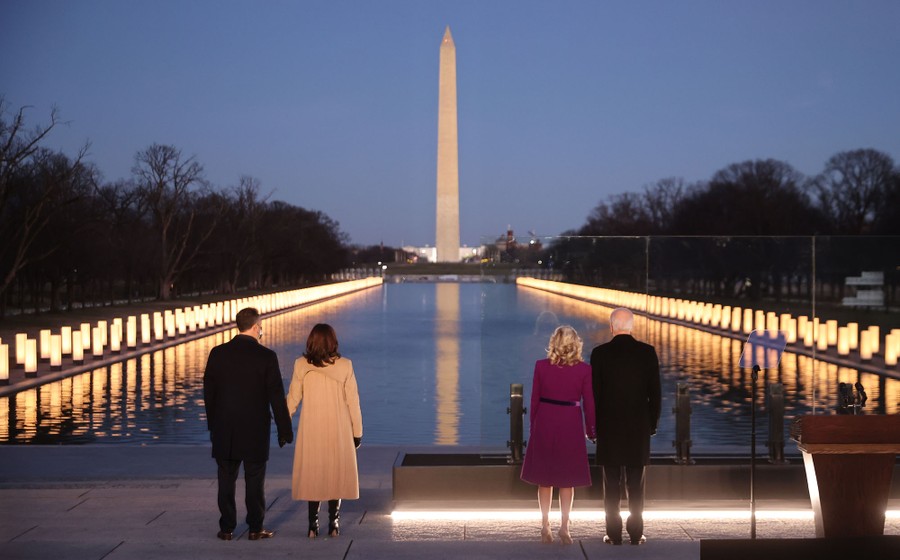 Joe Biden, Kamala Harris, and each of their spouses stand at the Lincoln Memorial Reflecting Pool, looking toward the Washington Monument and thousands of lanterns.