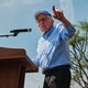 Bernie Sanders stands on a stage at a podium and points out