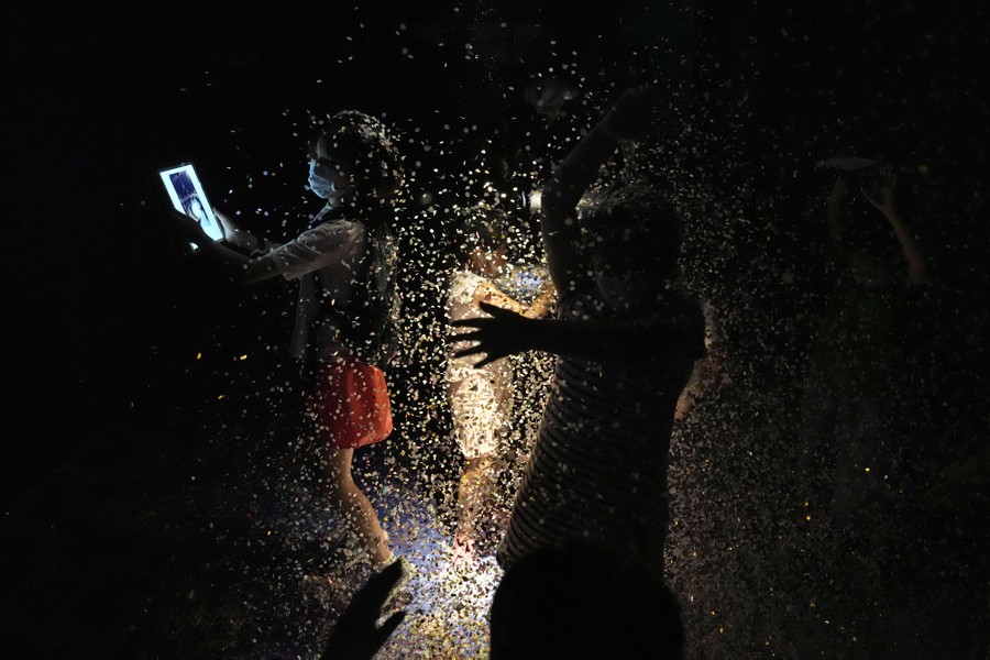 Children play in a dark room, surrounded by falling confetti.