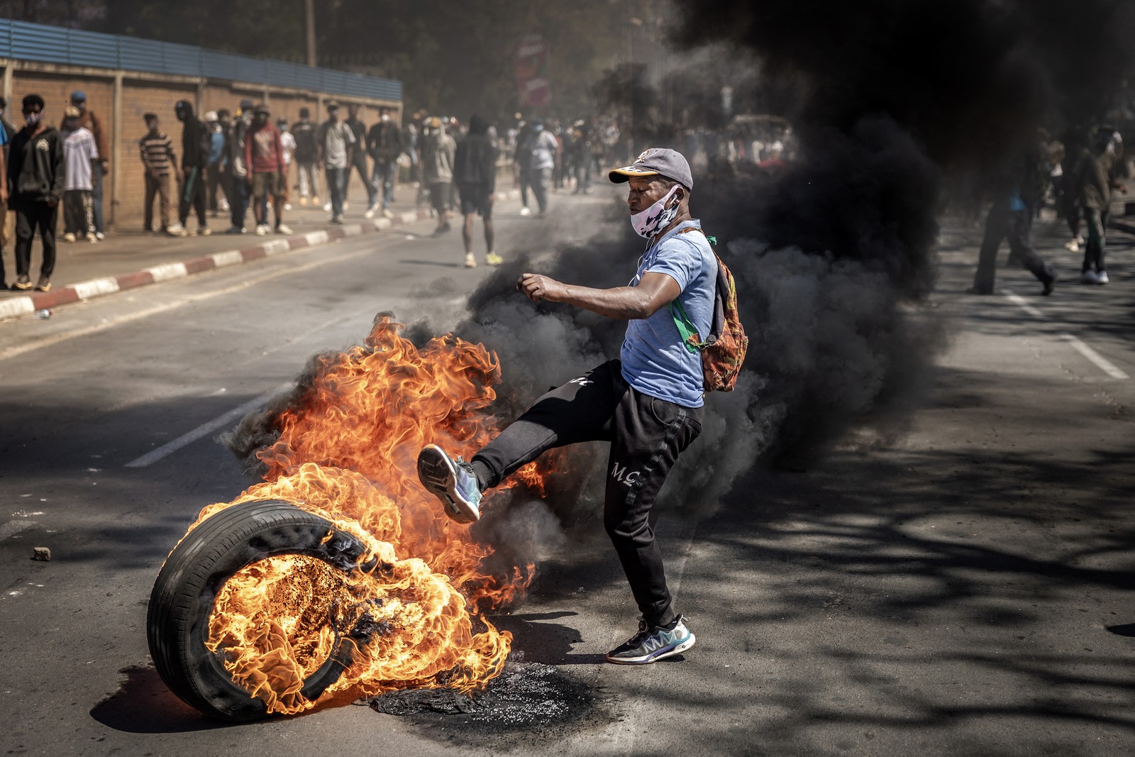 A protester kicks at a burning tire in the middle of a street.